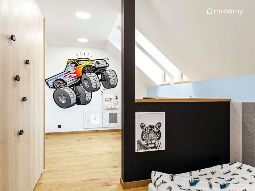 Pokój dla chłopca przedzielony ścianką działową ozdobioną plakatem z tygrysem a na ścianie białe organizery i tapeta z monster truckiem