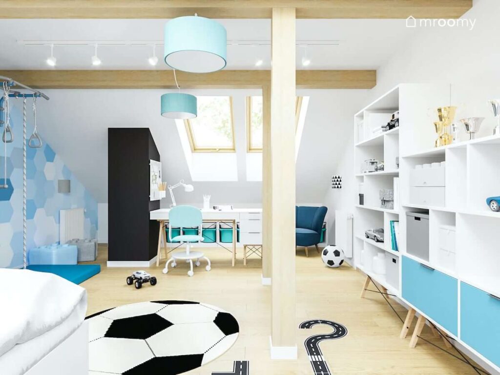 Jasny poddaszowy pokój dla chłopca z białymi regałami z niebieskimi elementami oraz małym biurkiem i dywanem w kształcie piłki