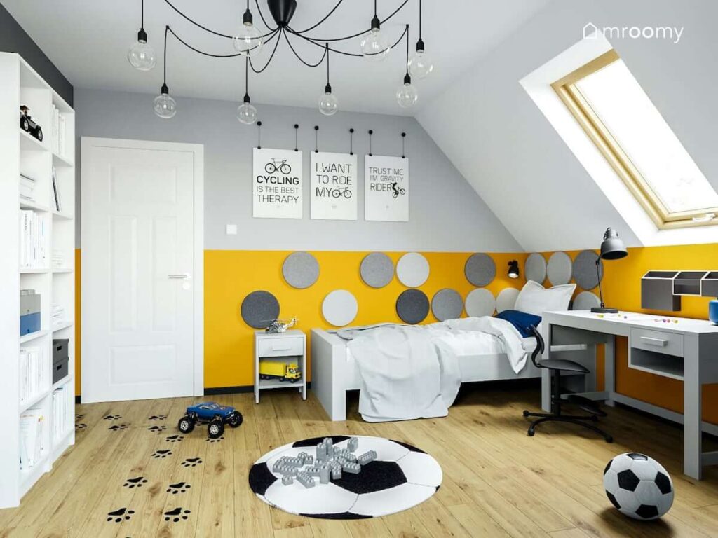 Szaro pomarańczowa ściana ozdobiona okrągłymi panelami ściennymi oraz łóżko i ozdobne plakaty na ścianie w pokoju chłopca na poddaszu
