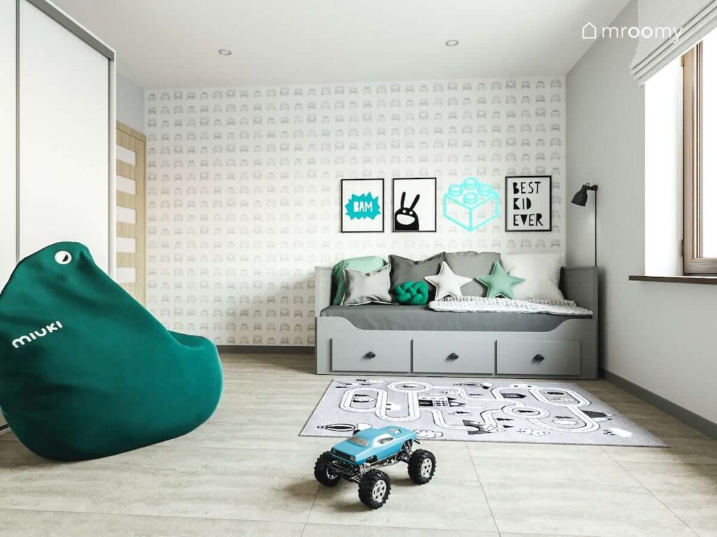 Rozkładane łóżko z szufladami oraz tapeta w samochody ozdobiona oprawionymi w ramki plakatami w pokoju chłopca