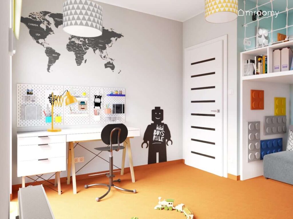 Białe biurko oraz komoda a na ścianie organizery naklejka w kształcie mapy świata oraz tablica kredowa w kształcie ludzika Lego w jasnym pokoju dla chłopca