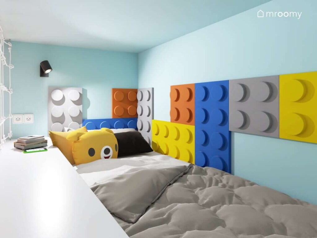 Łóżko na antresoli i ściany ozdobione kolorowymi panelami ściennymi w kształcie klocków Lego w biało niebieskim pokoju dla chłopca