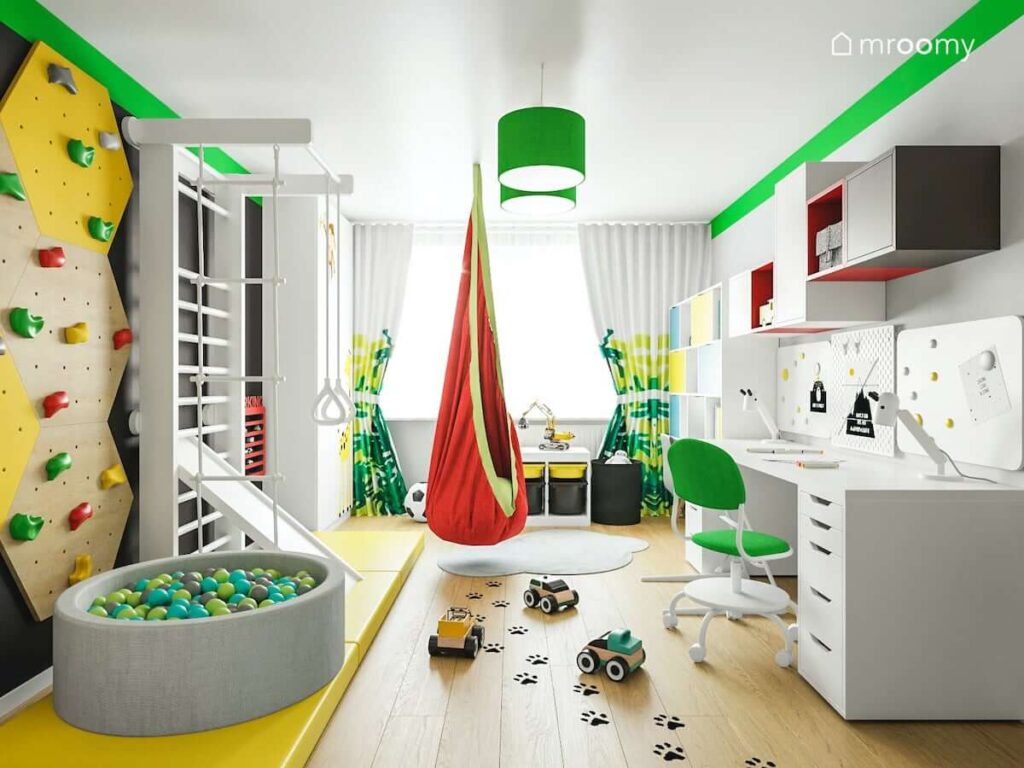 Basen z piłkami ścianka wspinaczkowa oraz drabinka gimnastyczna w strefie zabawy oraz biurko i kolorowe szafki w strefie nauki w pokoju dla dwóch chłopców
