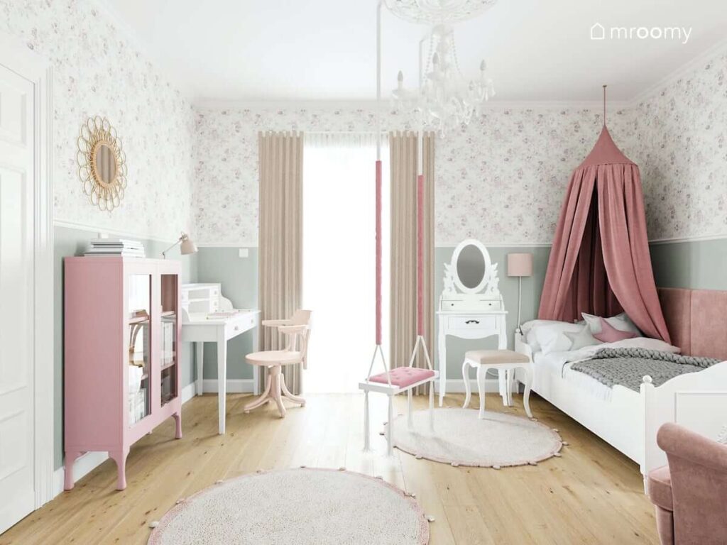Biało różowy pokój małej dziewczynki z łóżkiem ozdobionym baldachimem toaletką i dużym żyrandolem na środku pokoju zawieszona huśtawka