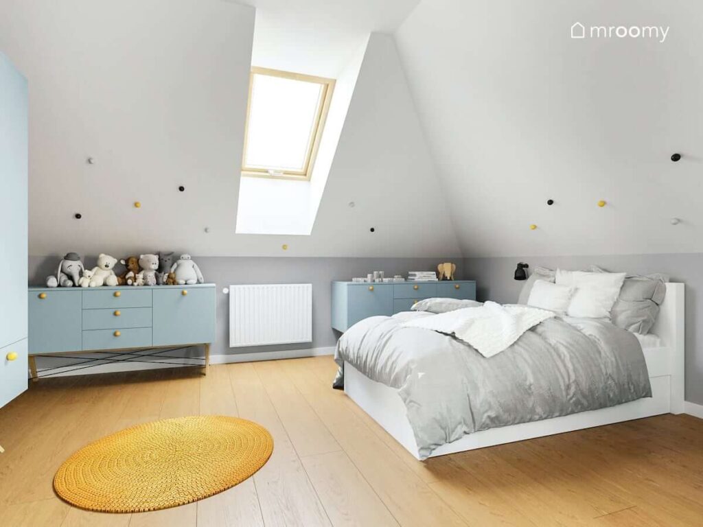 Poddaszowy pokój dla dziewczynki z dużym łóżkiem niebieskimi komodami oraz żółtym dywanem i ścianami udekorowanymi ozdobnymi gałkami