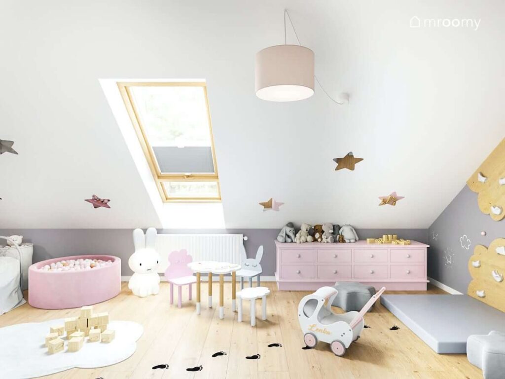 Sufit ozdobiony lustrzanymi gwiazdkami oraz stolik z krzesełkami w różnych kształtach i różowa komoda w poddaszowym pokoju dla dziewczynki