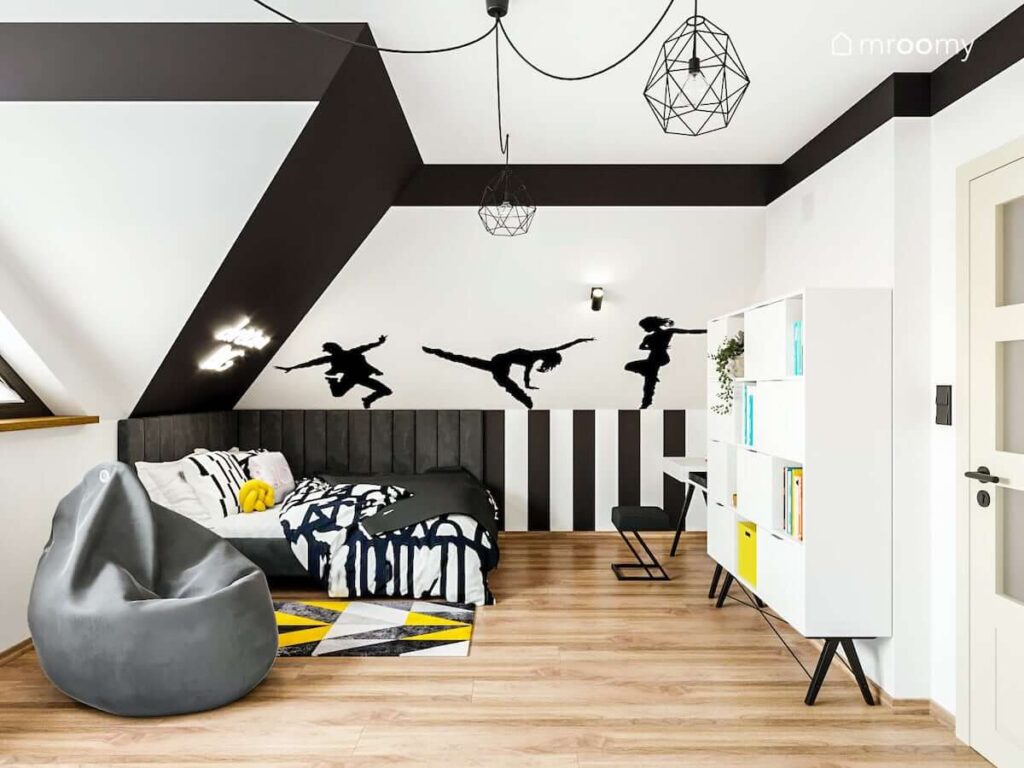 Czarno biały pokój nastolatki z łóżkiem uzupełnionym miękkimi panelami ściennymi oraz ścianą ozdobioną naklejkami w kształcie tancerek