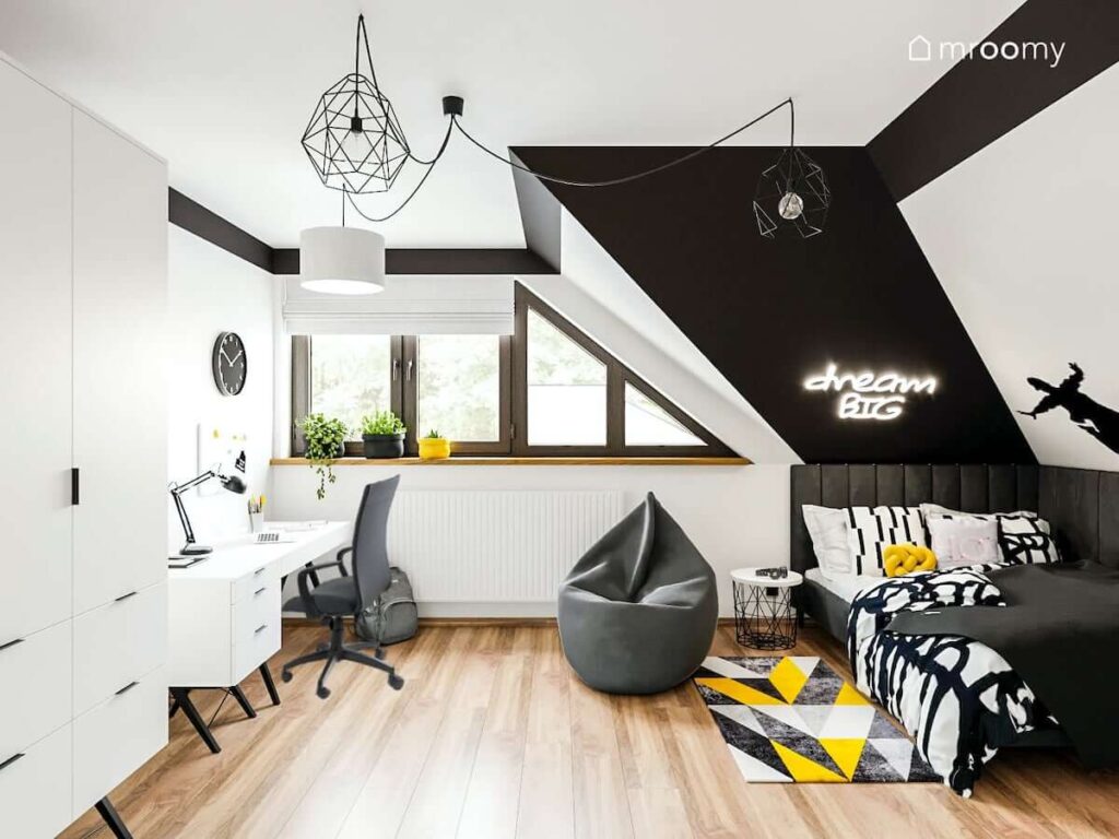 Czarno biały pokój dla nastolatki z biurkiem szafą oraz szarą pufą i kolorowym dywanem oraz świecącym napisem na ścianie