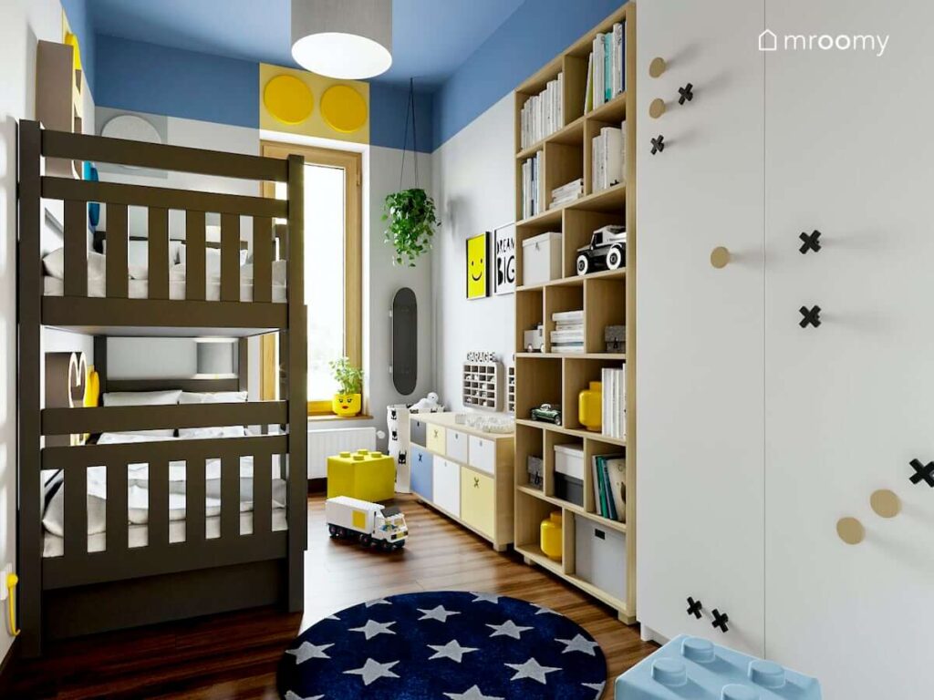 Kolorowy i radosny pokój dla rodzeństwa z piętrowym łóżkiem pojemną szafą i regałem oraz dywanem w gwiazdki i miękkimi panelami na ścianach