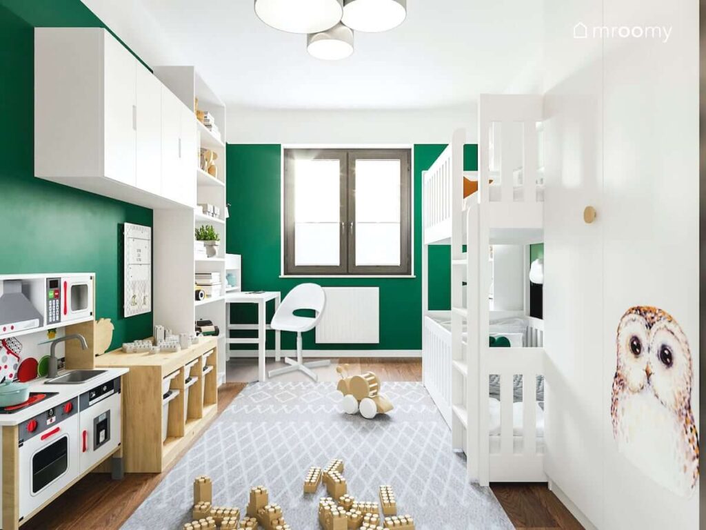 Białe łóżko piętrowe oraz biały regał szafki i biurko oraz kuchnia dla dzieci w zielonym pokoju dla rodzeństwa