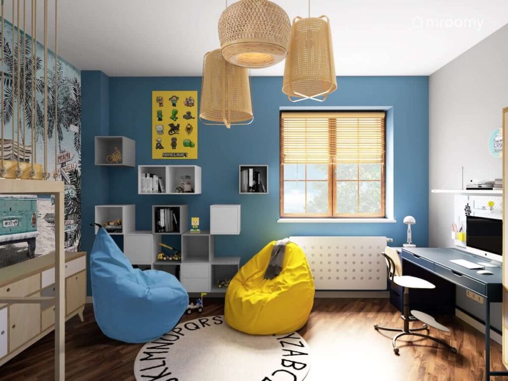 Pokój chłopca z intensywnie niebieską ścianą okrągłym dywanem z literkami i workami sako niebieskim biurkiem i modułowymi kwadratowymi półkami i bambusowymi lampami