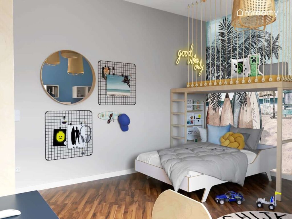 Pokój dla nastolatka w kolorystyce szaro-niebieskiej utrzymany w wakacyjnym klimacie z przestrzenią na antresoli meblami ze sklejki i ledonem i okrągłym lustrem i metalowymi organizerami na ścianie