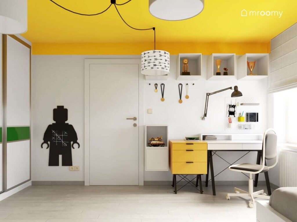 Pokój dla nastoletniego sportowca i fana gier komputerowych w kolorystyce biało-żółtej z czarnymi dodatkami z żółtym sufitem i nowoczesnym biurkiem skandynawskim