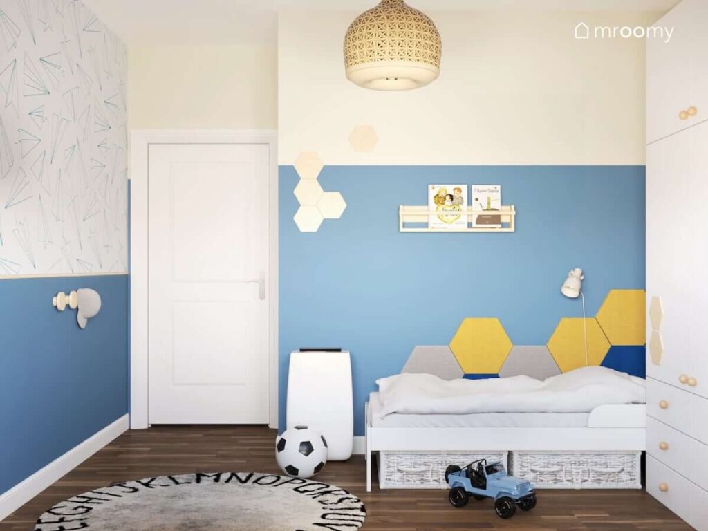 Beżowo niebieski pokój dla chłopca z tapetą w papierowe samoloty na jednej ze ścian oraz miękkimi panelami ściennymi przy łóżku