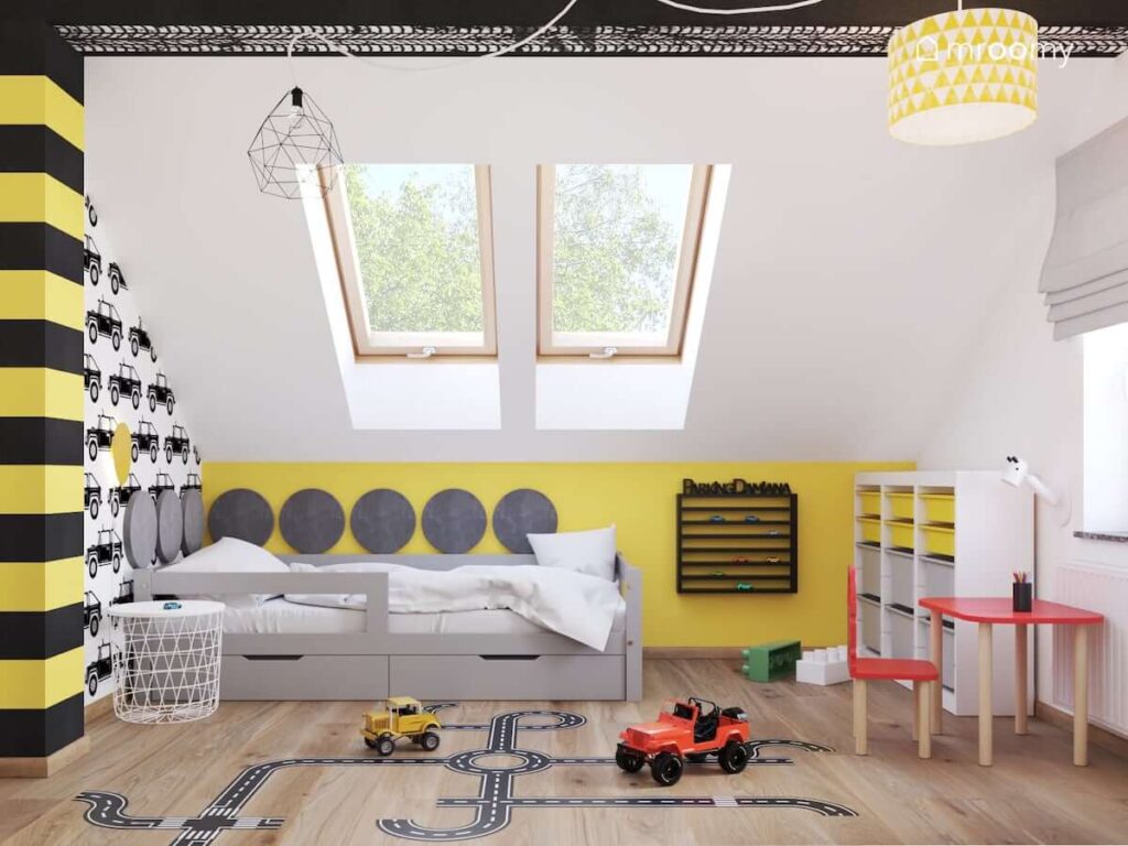 Czarno biało żółty pokój ze skosami dla chłopca z tapetą w samochody łóżkiem z szufladami naklejką podłogową w kształcie jezdni oraz naklejką w kształcie śladów opon na suficie