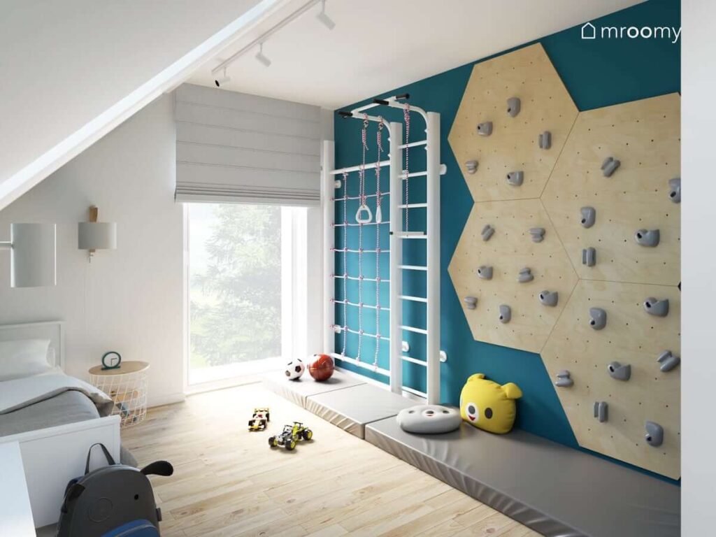 Ścianka wspinaczkowa oraz drabinka gimnastyczna i materace w pokoju dla chłopca z niebieską ścianą