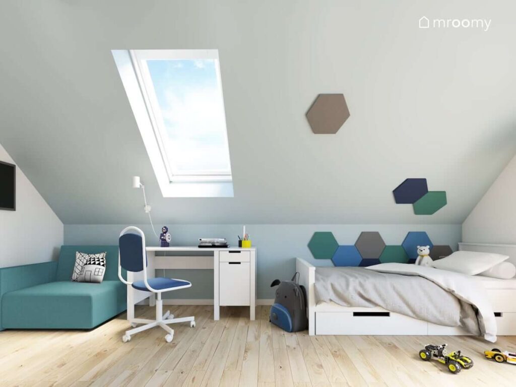 Biało niebieski poddaszowy pokój dla chłopca z łóżkiem biurkiem oraz małą sofą a także ścianą ozdobioną miękkimi panelami ściennymi w kształcie heksagonów