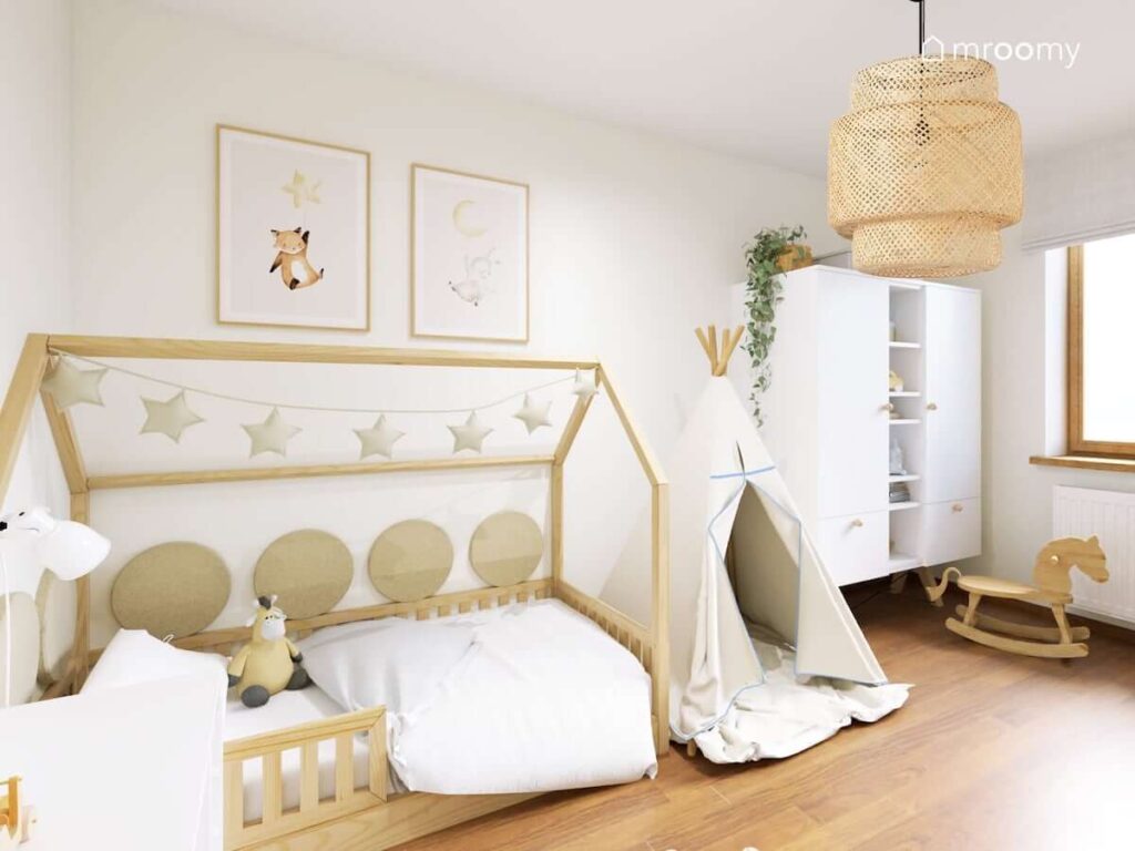 Drewniane łóżko w kształcie domku ozdobione girlandą gwiezdną i miękkimi panelami ściennymi oraz biała szafa i namiot do zabawy w jasnym pokoju małego chłopca