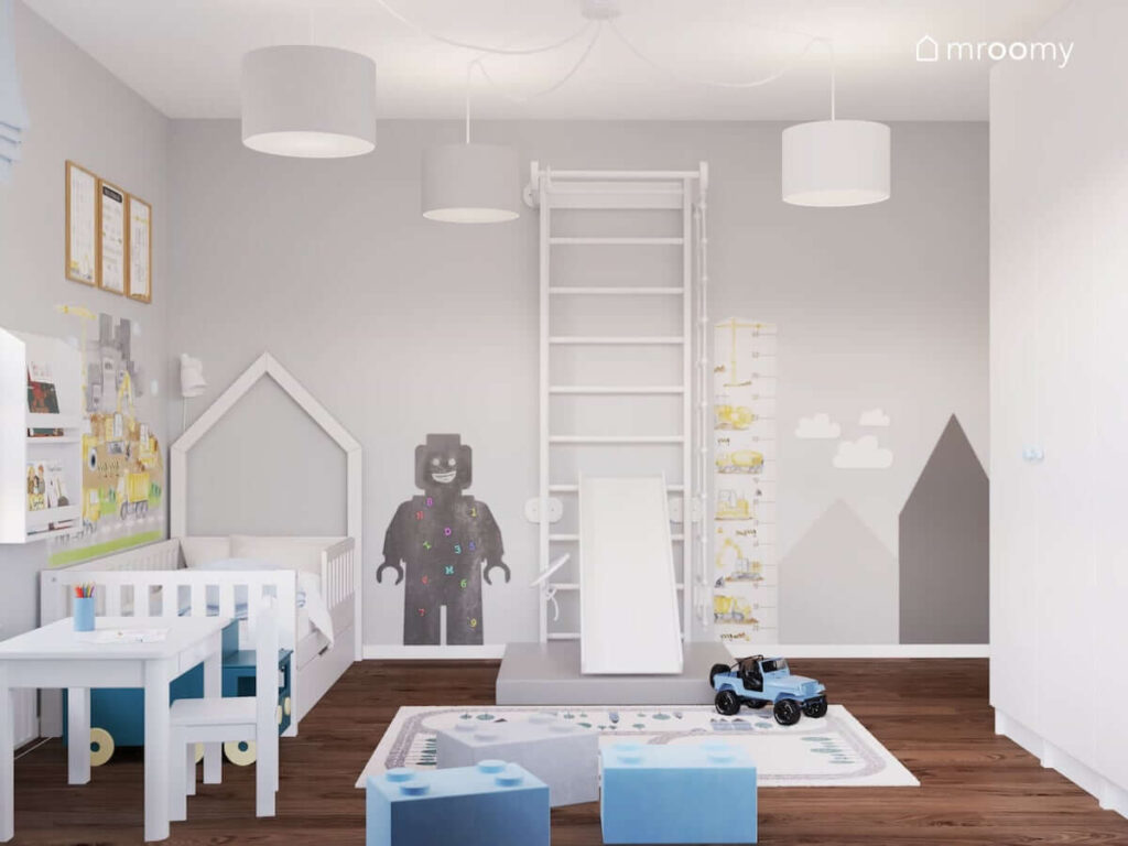 Białe łóżko oraz drabinka gimnastyczna a na ścianach liczne tablice kredowe w różnych kolorach i kształtach w pokoju małego chłopca