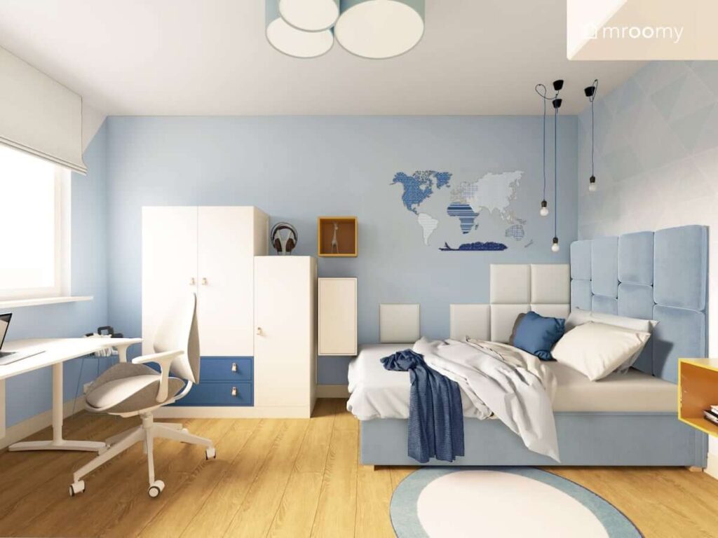 Biało niebieski pokój dla chłopca z naklejką w kształcie mapy i miękkimi panelami ściennymi na ścianie oraz niebieskim łóżkiem i białymi szafami i biurkiem pod oknem