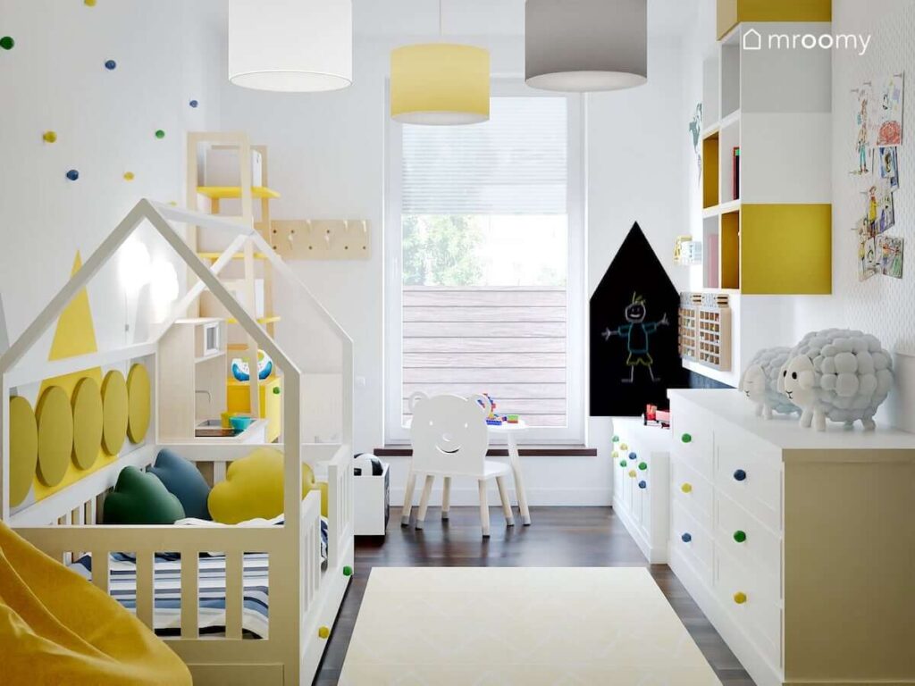 Pokój dla małego chłopca z łóżkiem w kształcie domku komodami z kolorowymi gałkami oraz żółto szaro białymi półkami ściennymi i takimi samymi lampami sufitowymi