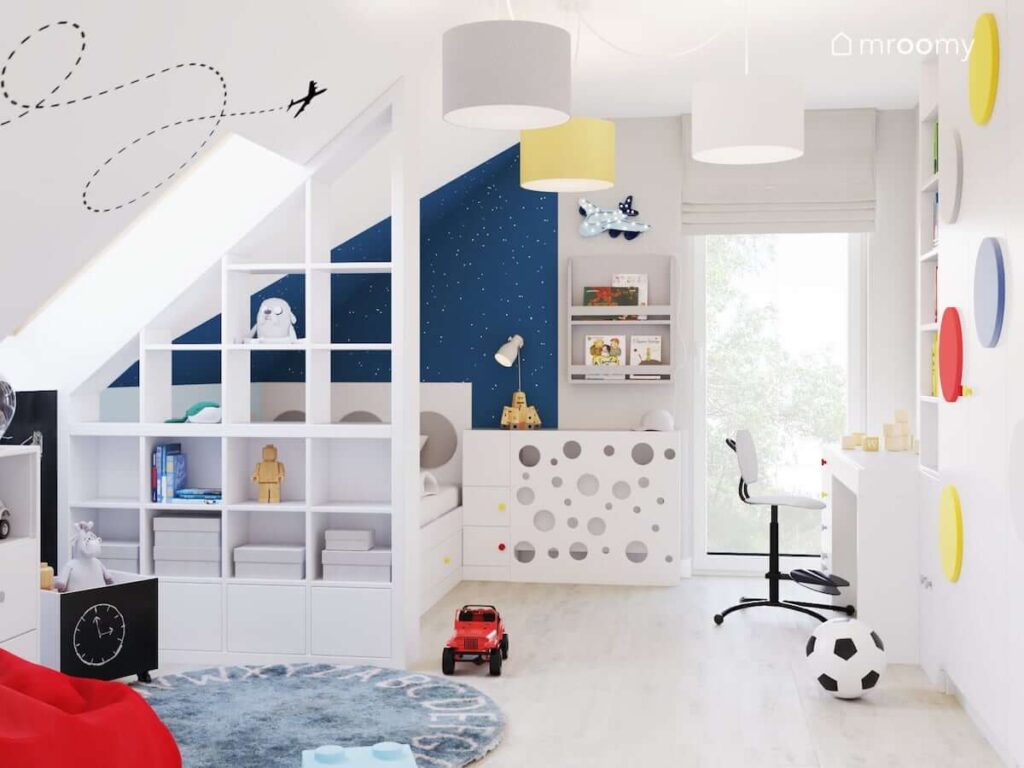 Poddaszowy pokój dla chłopca w jasnych kolorach z lampa sufitową z trzema abażurami naklejką ścienną oraz lampką nocną w kształcie samolotu i niebieskim dywanem z alfabetem