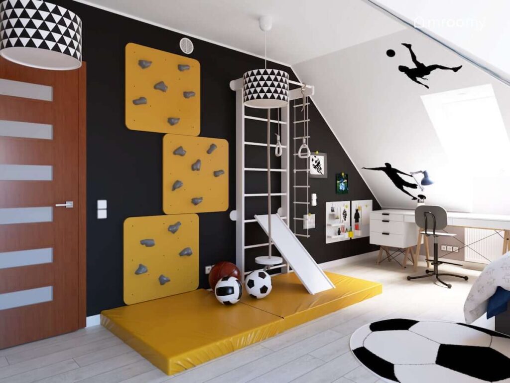 Czarna ściana z drabinką gimnastyczną żółtą ścianką wspinaczkową i organizerami ściennymi a u sufitu lampy z abażurami w trójkąty w poddaszowym pokoju dla chłopca