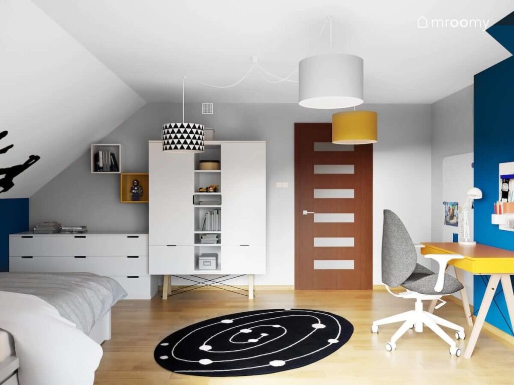 Pokój dla chłopca z białą szafą i komodą oraz musztardowym biurkiem a także dywanem w galaktyczny wzór