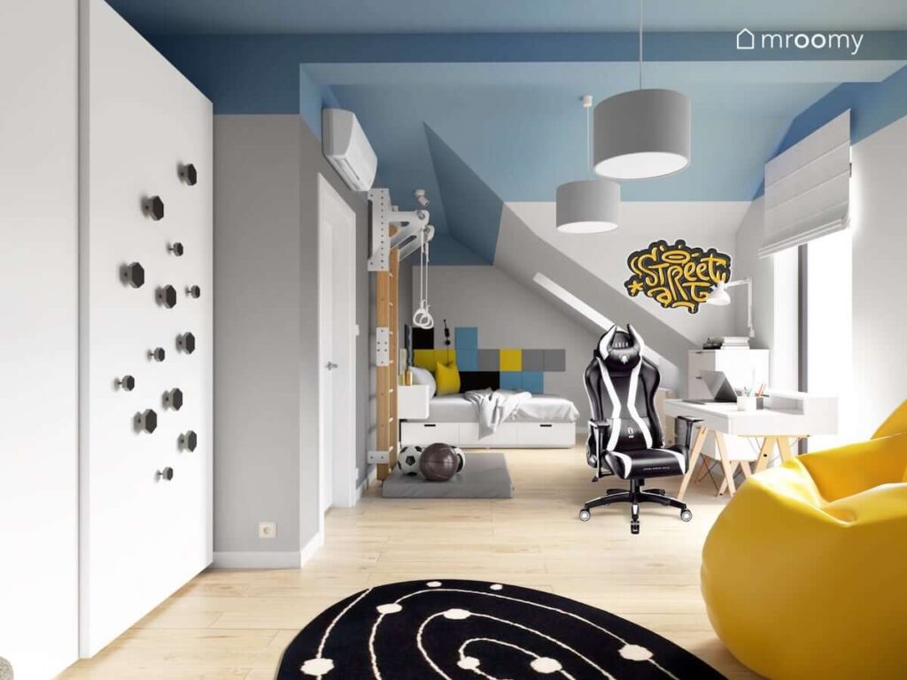 Pokój na poddaszu dla nastolatka z fotelem gamingowym błękitnym sufitem z drabinką gimnastyczną czarnym okrągłym dywanem żółtą pufą sako kolorowymi piankowymi panelami na ścianie