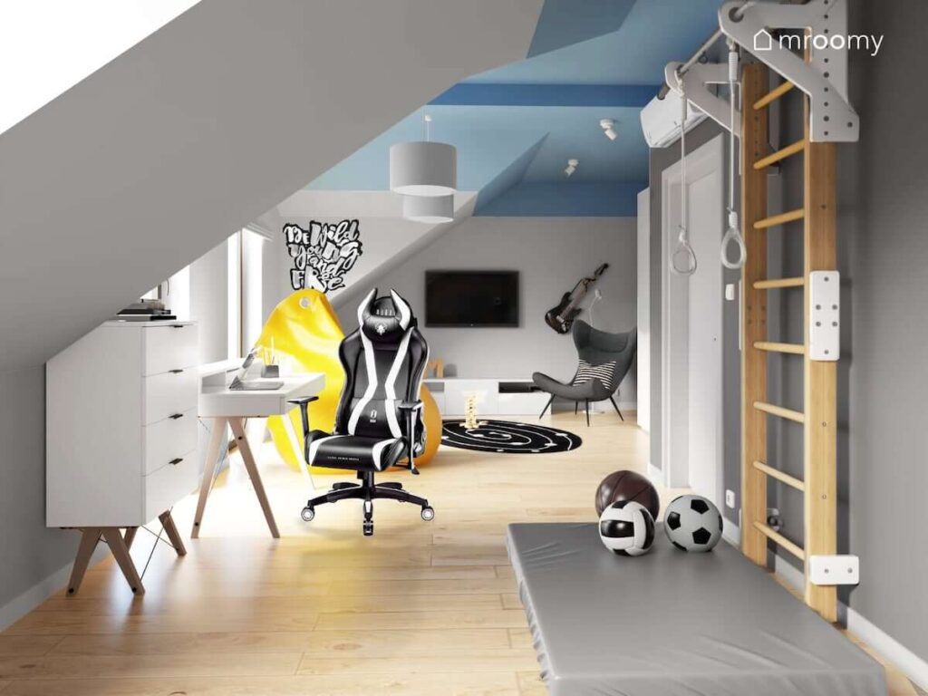 Pokój dla nastolatka z białymi meblami z drabinką gimnastyczną fotelem gamingowym białym skandynawskim biurkiem z nadstawką na drewnianych nogach z uchwytem na gitarę elektryczną telewizorem i żółtym workiem sako z graffiti na ścianie