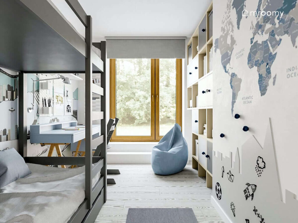 Wąski pokój dla dwóch braci z szarym łóżkiem piętrowym błękitną pufą sako biurkiem skandynawskim na drewnianych nogach ozdobiony naklejką przedstawiającą mapę świata