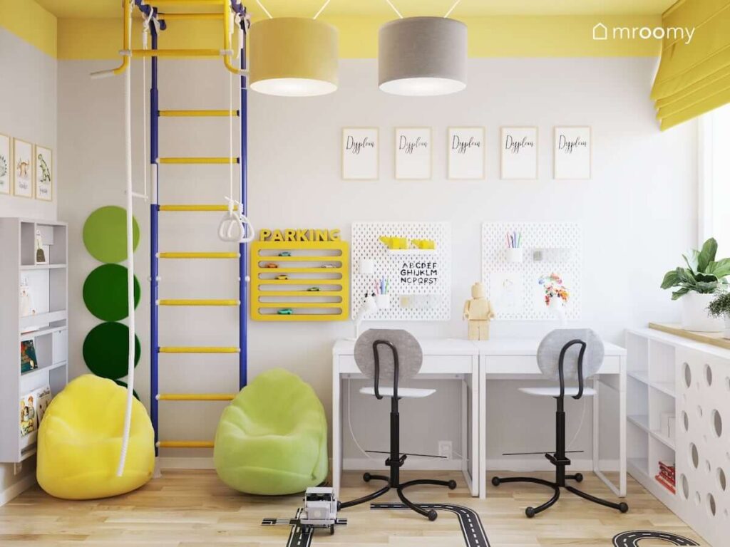 Dwa biurka drabinka gimnastyczna kolorowe pufy a na ścianie półka na samochody oraz organizery ścienne w pokoju dla dwóch chłopców z żółtym sufitem i białymi ścianami