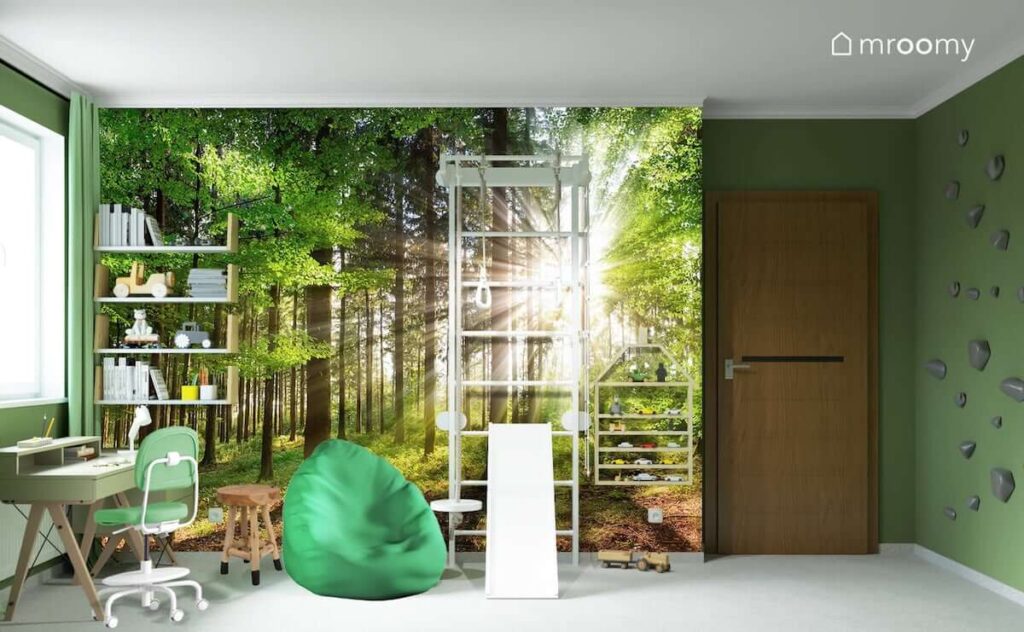 Fototapeta przedstawiająca las oraz drewniane półki ścienne drabinka gimnastyczna i zielona pufa sako a na ścianie uchwyty wspinaczkowe w pokoju dla chłopca