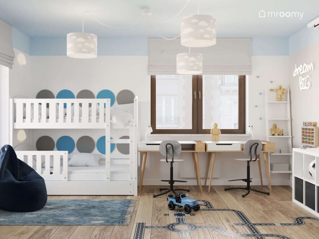Biało niebieski pokój dla rodzeństwa z białym łóżkiem piętrowym oraz drewnianymi biurkami i lampą sufitową z szarymi abażurami w chmurki