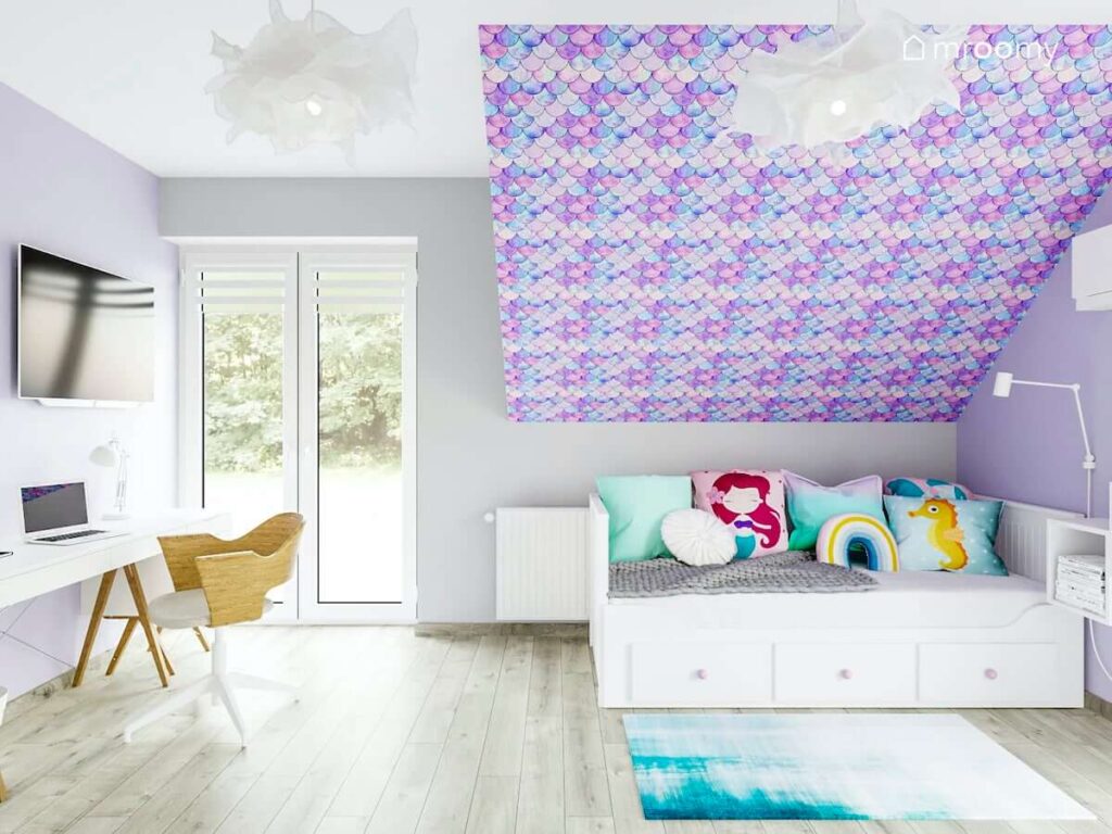 Pokój dla dziewczynki na poddaszu z łóżkiem pod skosem z białymi meblami z fioletowymi gałkami tapetą na ścianie ze skosem dekoracjami nawiązującymi do bajki mała syrenka z fioletowo-różowo-morską tapetą imitującą łuski na syrenim ogonie