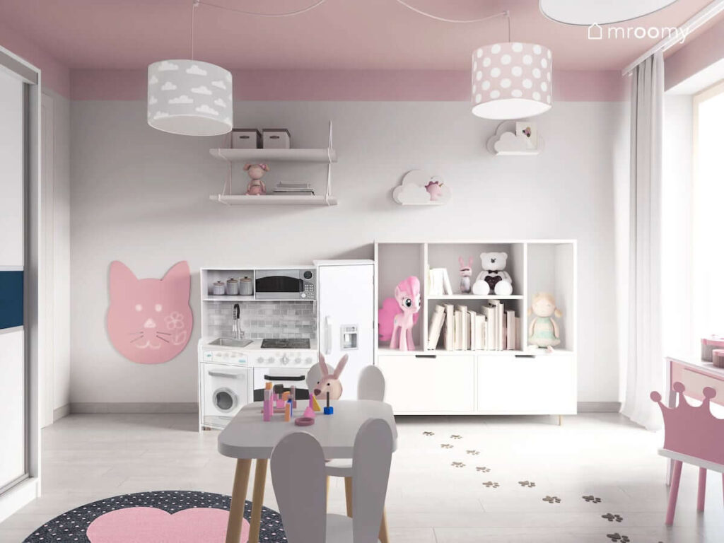 Przestronny pokój na małej dziewczynki w kolorystyce szaro-różowej z białymi meblami czarno-różowym dywanem tablicą suchościeralną w kształcie królika i stoliczkiem z krzesełkami
