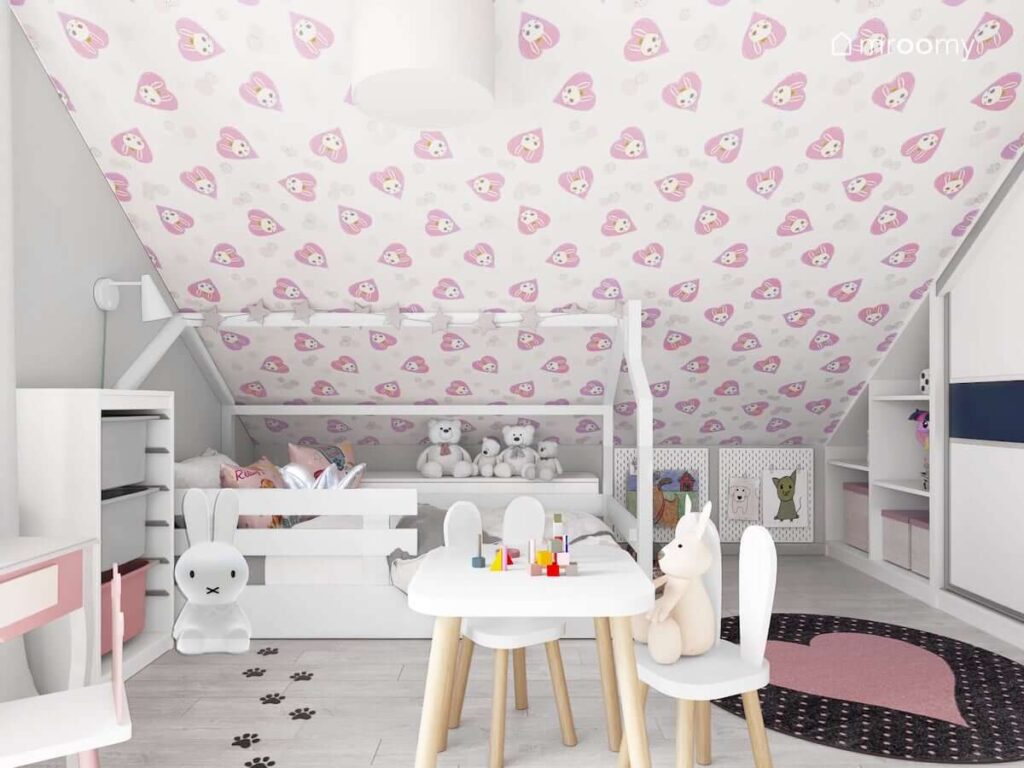 Białe łóżko domek pod skosem w pokoju fanki królików z dywanem z różowym sercem i lampą w kształcie królika i białymi meblami