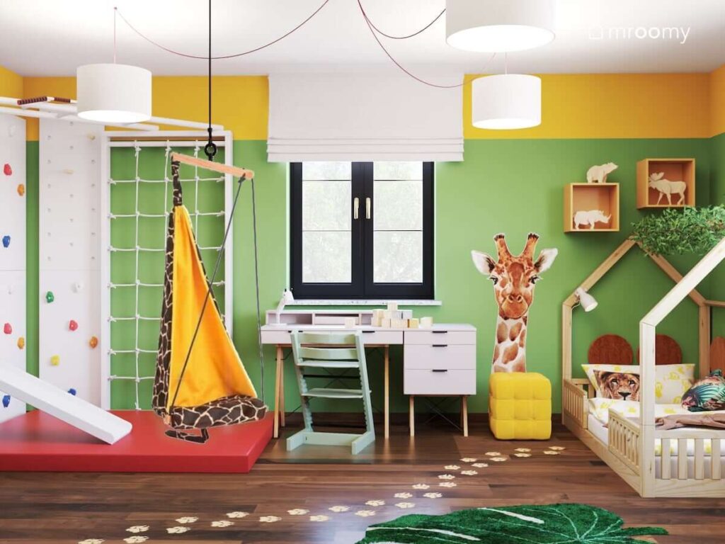 Zielono żółty pokój dla dziewczynki z drabinką gimnastyczną ze ścianką wspinaczkową fotelem wiszącym w kształcie żyrafy oraz naklejką ścienną z żyrafą