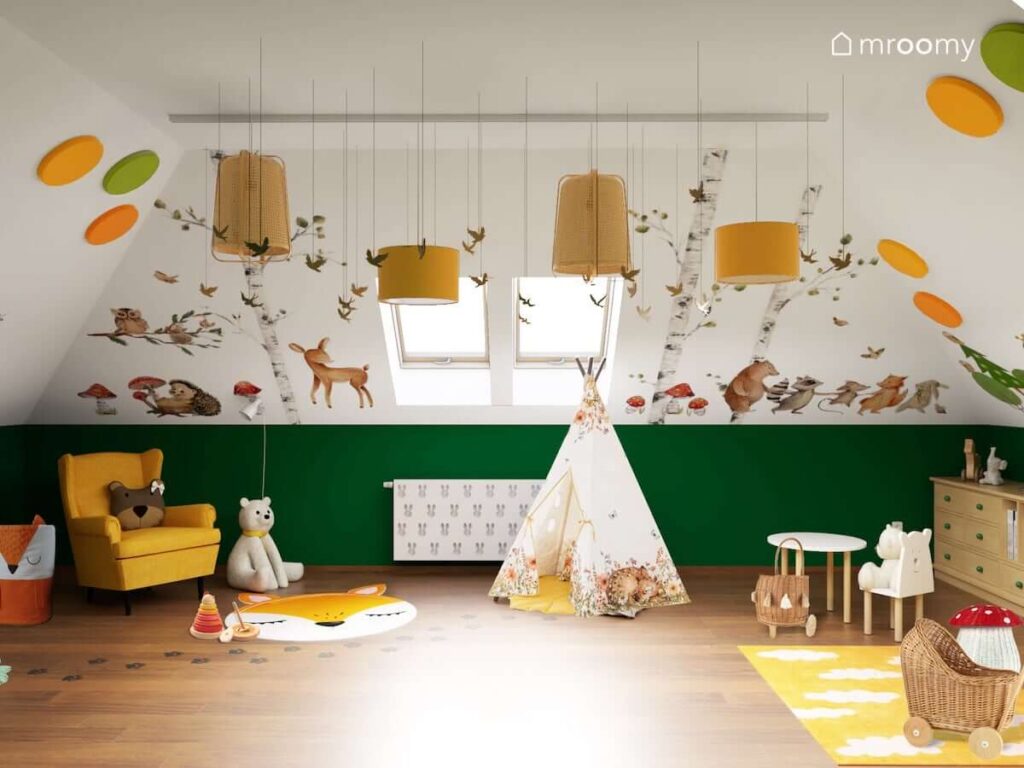 Leśny pokój na poddaszu dla małego dziecka z dużą przestrzenią do zabawy kącikiem plastycznym dodatkami w kolorach żółtym i pomarańczowym leśnymi naklejkami na ścianach bambusowymi lampami sufitowymi osłoną na kaloryfer i żółtym fotelem do karmienia