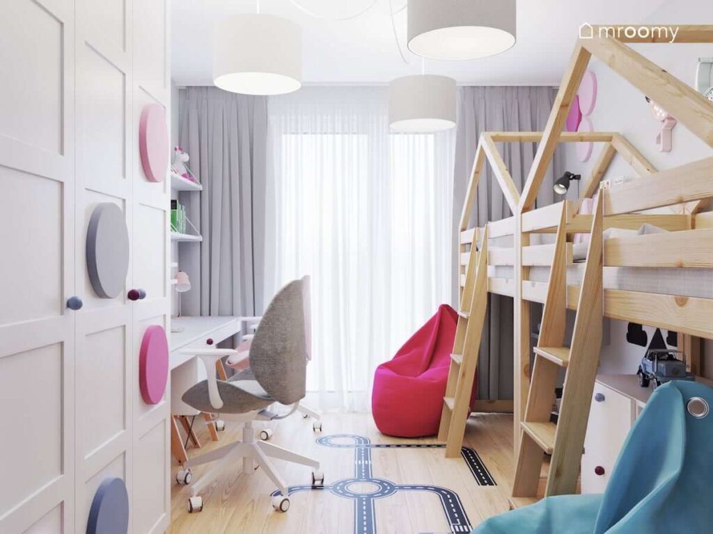Mały pokój dla rodzeństwa z dwoma biurkami łóżkami na drewnianych antresolach oraz pufami sako a także dużą szafą ozdobioną panelami ściennymi w różnych kolorach