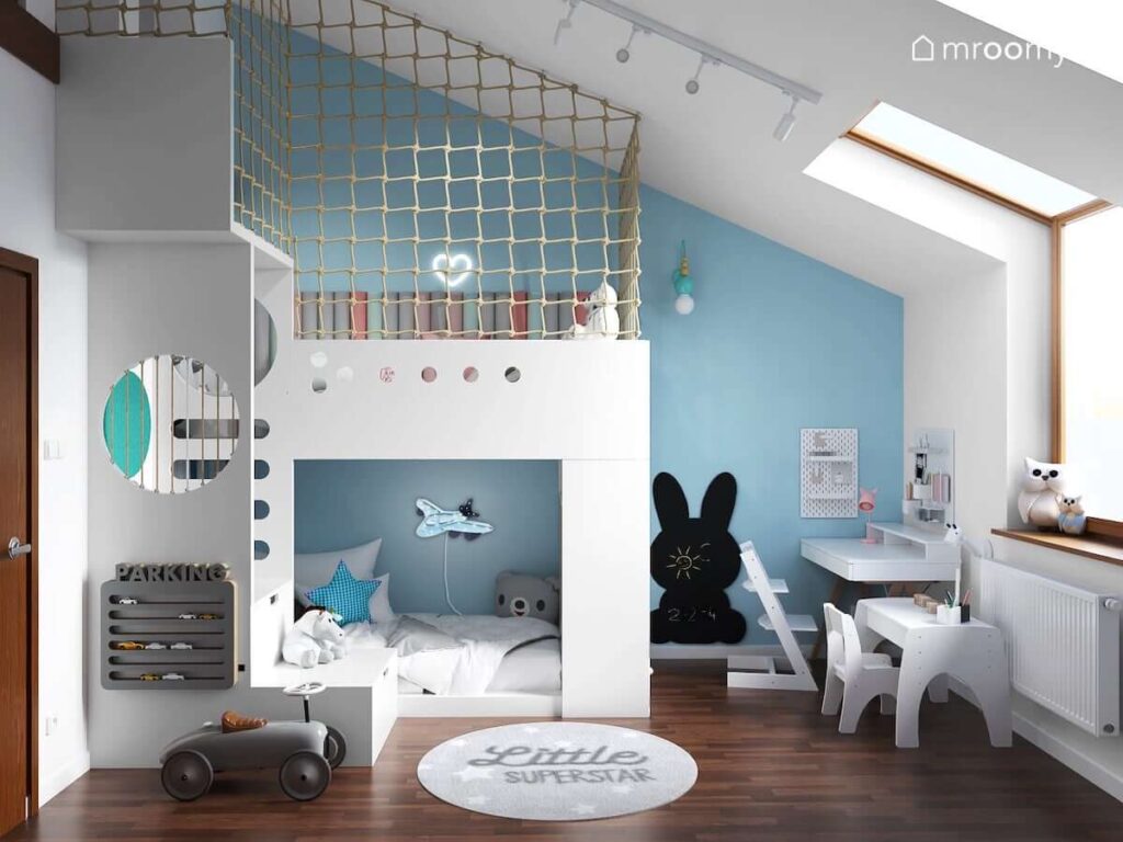 Biało niebieski pokój ze skosami dla rodzeństwa z piętrowym łóżkiem w formie antresoli oraz tablicą kredową w kształcie królika oraz biurkiem i stolikiem dziecięcym