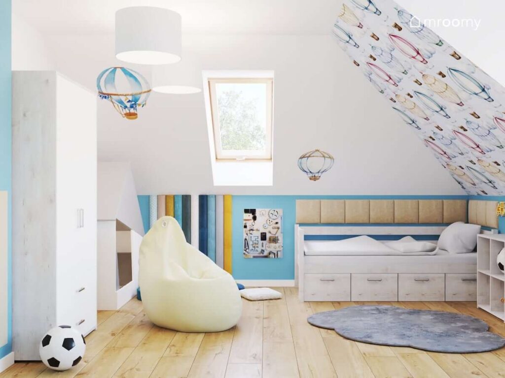 Pokój dla kilkuletniego chłopca z bielonymi meblami jasną pufą sako dywanem w kształcie chmurki oraz ścianami ozdobionymi kolorowymi panelami ściennymi oraz tapetą i naklejkami w balony