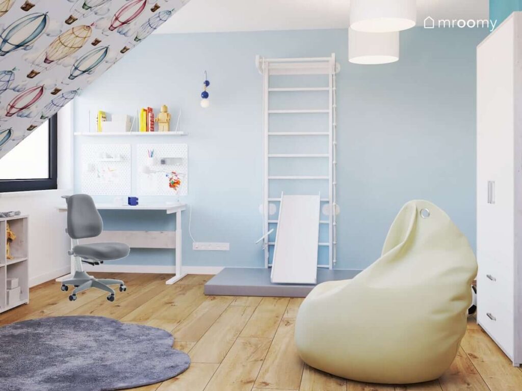 Biało niebieski pokój dla chłopca z drabinką gimnastyczną jasną pufą sako oraz biurkiem z organizerami ściennymi i półką