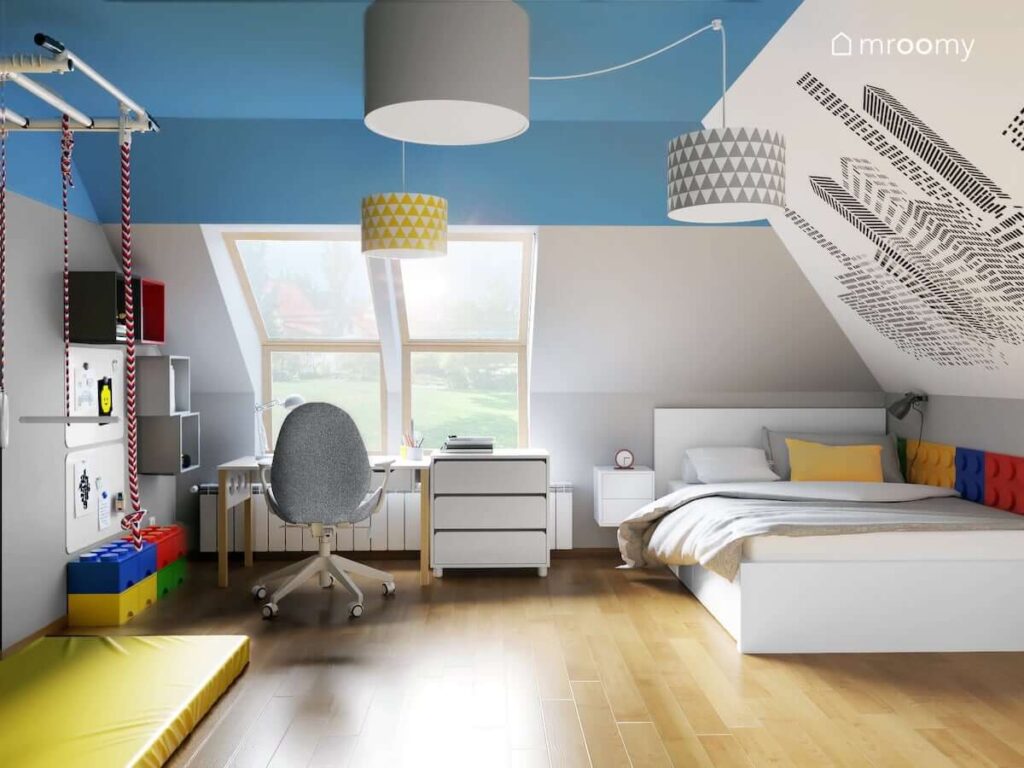 Biało niebieski pokój dla chłopca w wieku szkolnym z białymi meblami tapetą z graficznymi wieżowcami na skosie oraz kolorowymi szafkami ściennymi i pojemnikami na klocki Lego