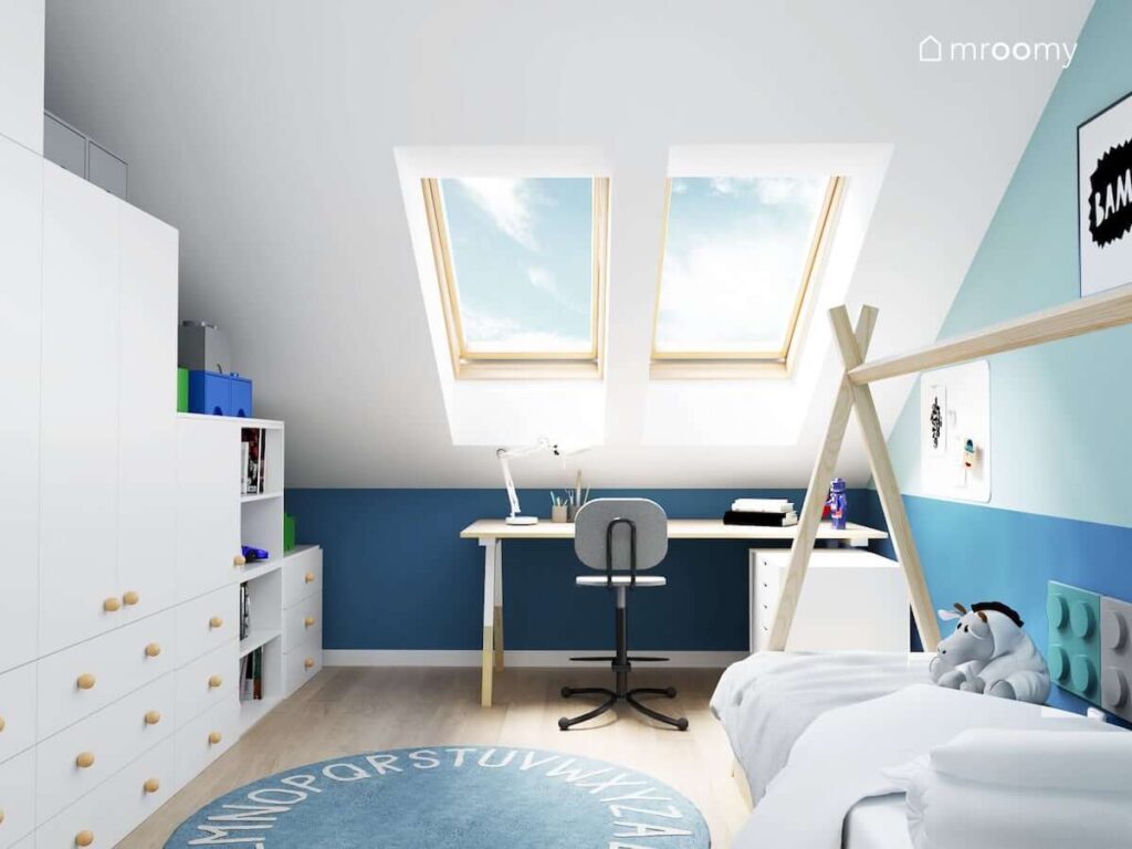 Jasny poddaszowy pokój dla chłopca z białą szafą modułową drewnianym biurkiem i niebieskim dywanem z alfabetem