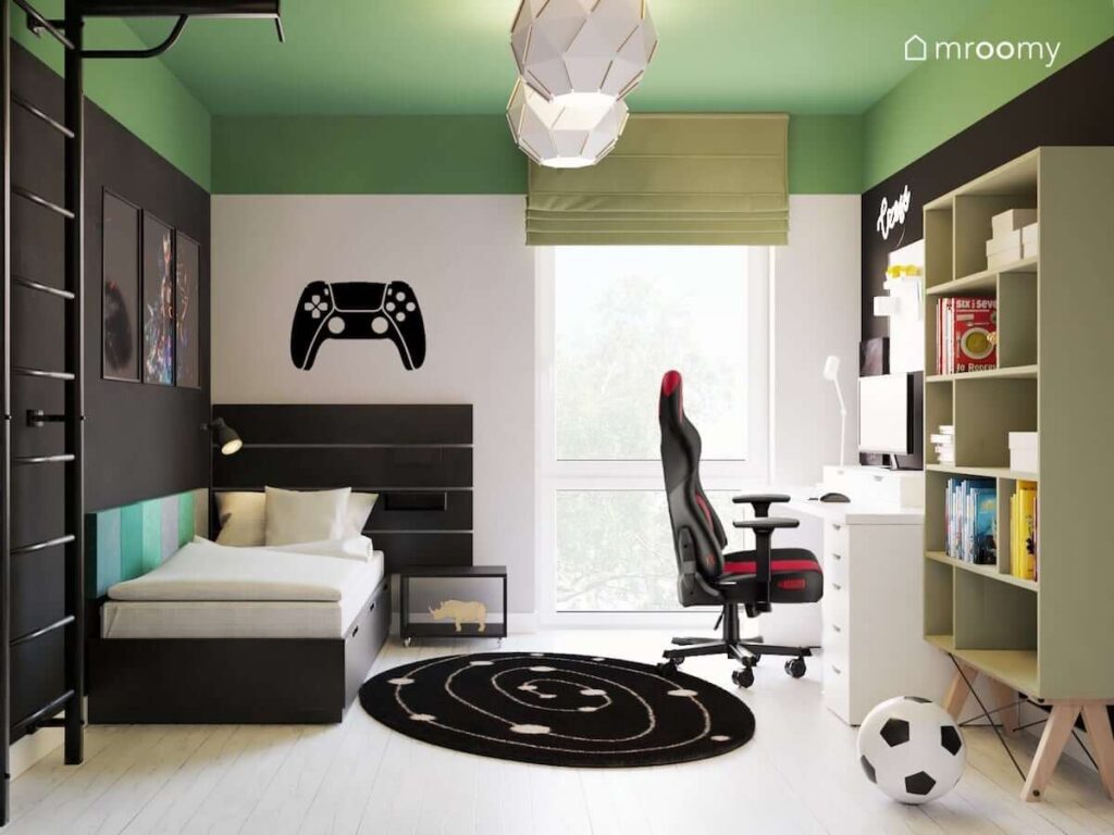Zielono biało czarny pokój dla fana gier komputerowych z łóżkiem z dużym funkcjonalnym zagłówkiem i naklejką w kształcie pada na ścianie a także czarno białym dywanem i ozdobnymi lampami sufitowymi