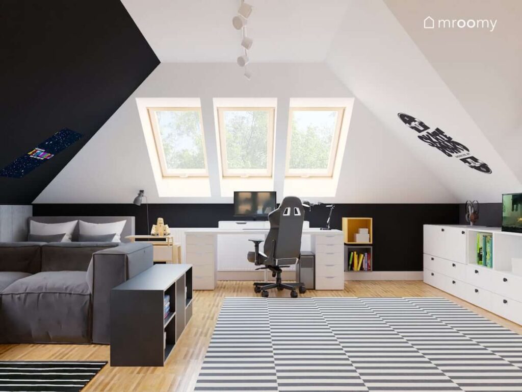 Biało czarny poddaszowy pokój dla nastolatka z dużymi dywanami w paski podwójnym łóżkiem i sofą oraz dużym biurkiem z fotel gamingowym pod oknem