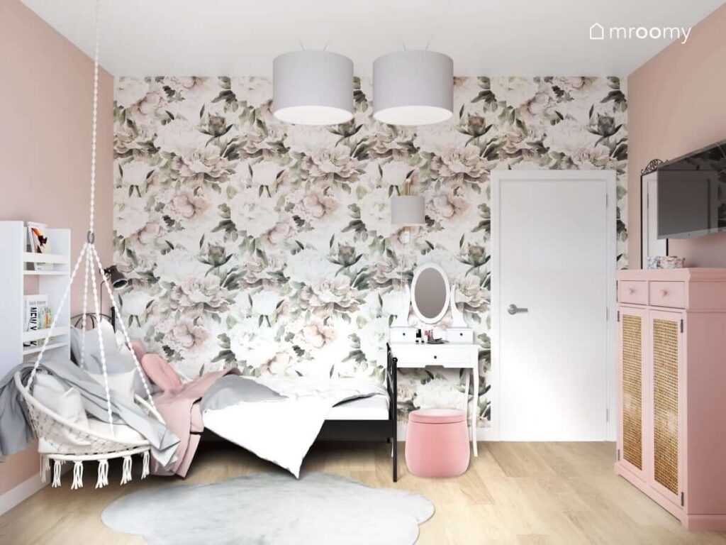 Czarne metalowe łóżko fotel wiszący oraz biała toaletka i różowa pufa z pojemnikiem a na ścianie tapeta w piwonie w pokoju dla dziewczynki
