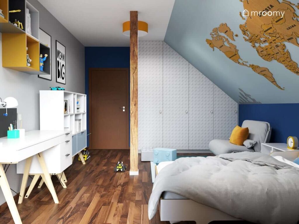 Białe meble na drewnianych nogach oraz białe łóżko i szafa oklejona naklejką z wzorem klocka Lego a na ścianach ozdobne plakaty drewniana mapa świata i szafki w różnych kolorach w pokoju dla chłopca