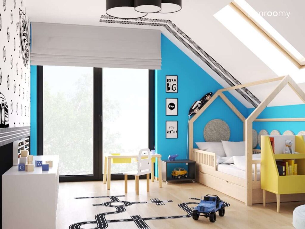 Biało niebieski pokój dla chłopca z drewnianym łóżkiem domkiem stolikiem do zabawy z krzesełkiem z oparciem w kształcie auta oraz lampką nocną w kształcie wyścigówki